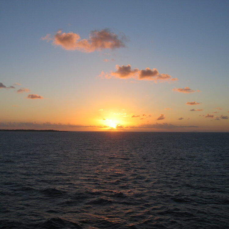 Sunset over calm ocean with clouds.