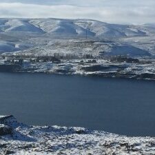 Snowy hills and lake under cloudy sky.