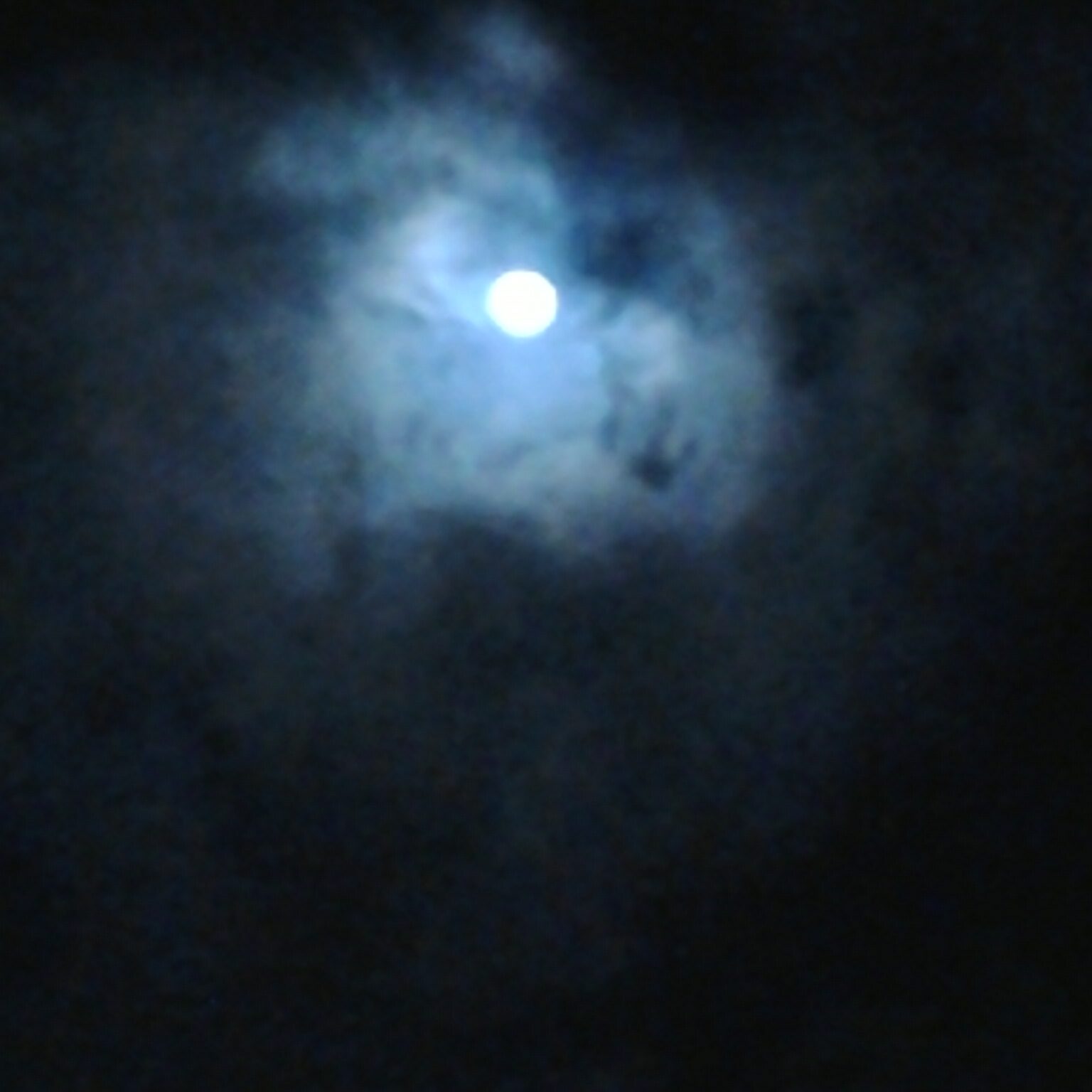 Moon shining through dark, cloudy sky.