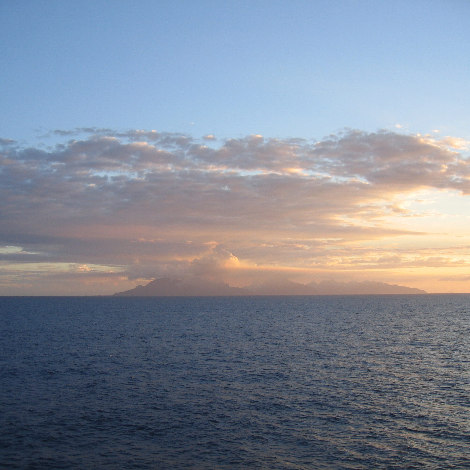 Ocean sunset with distant cloudy island view.