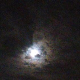 Moon shining through dark, cloudy night sky.