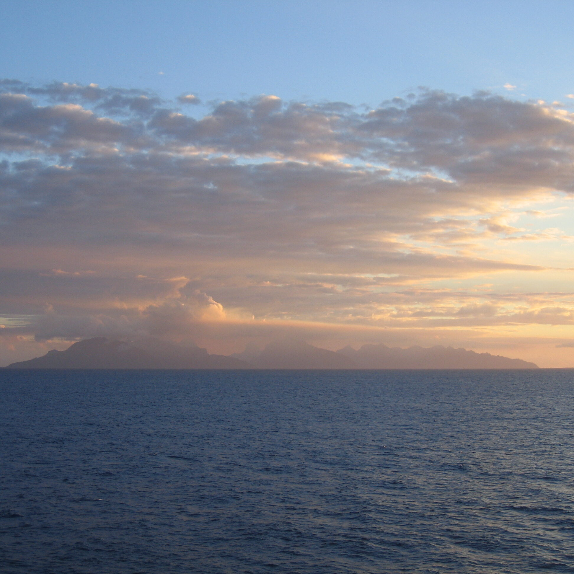 Distant island under cloudy sunrise sky.