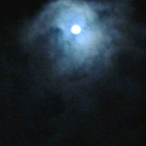 Full moon shining through cloudy night sky.