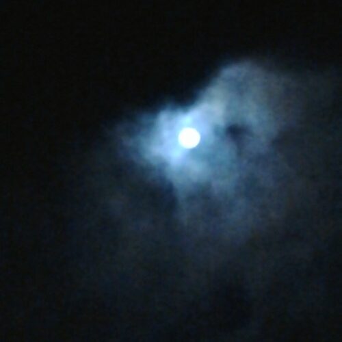 Moon shining through dark, cloudy night sky.