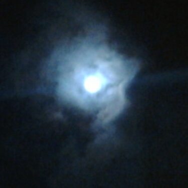 Bright moon surrounded by dark, wispy clouds.