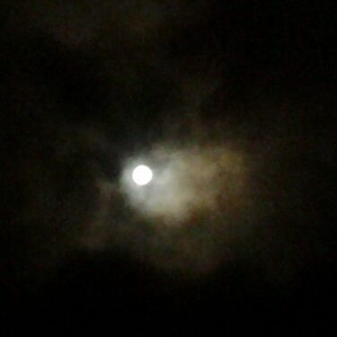 Bright moon surrounded by dark, wispy clouds.