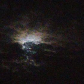 Moonlight peeking through dark, cloudy sky.