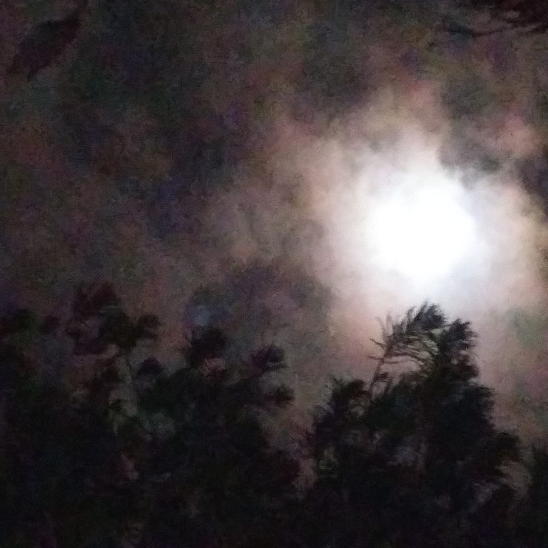 Moon shining through cloudy night sky.