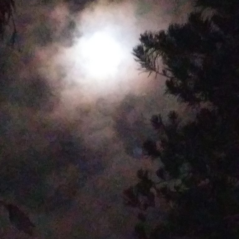 Moon shining through cloudy night sky.