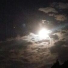 Bright moon shining through cloudy night sky.