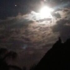 Bright moon shining through cloudy night sky.