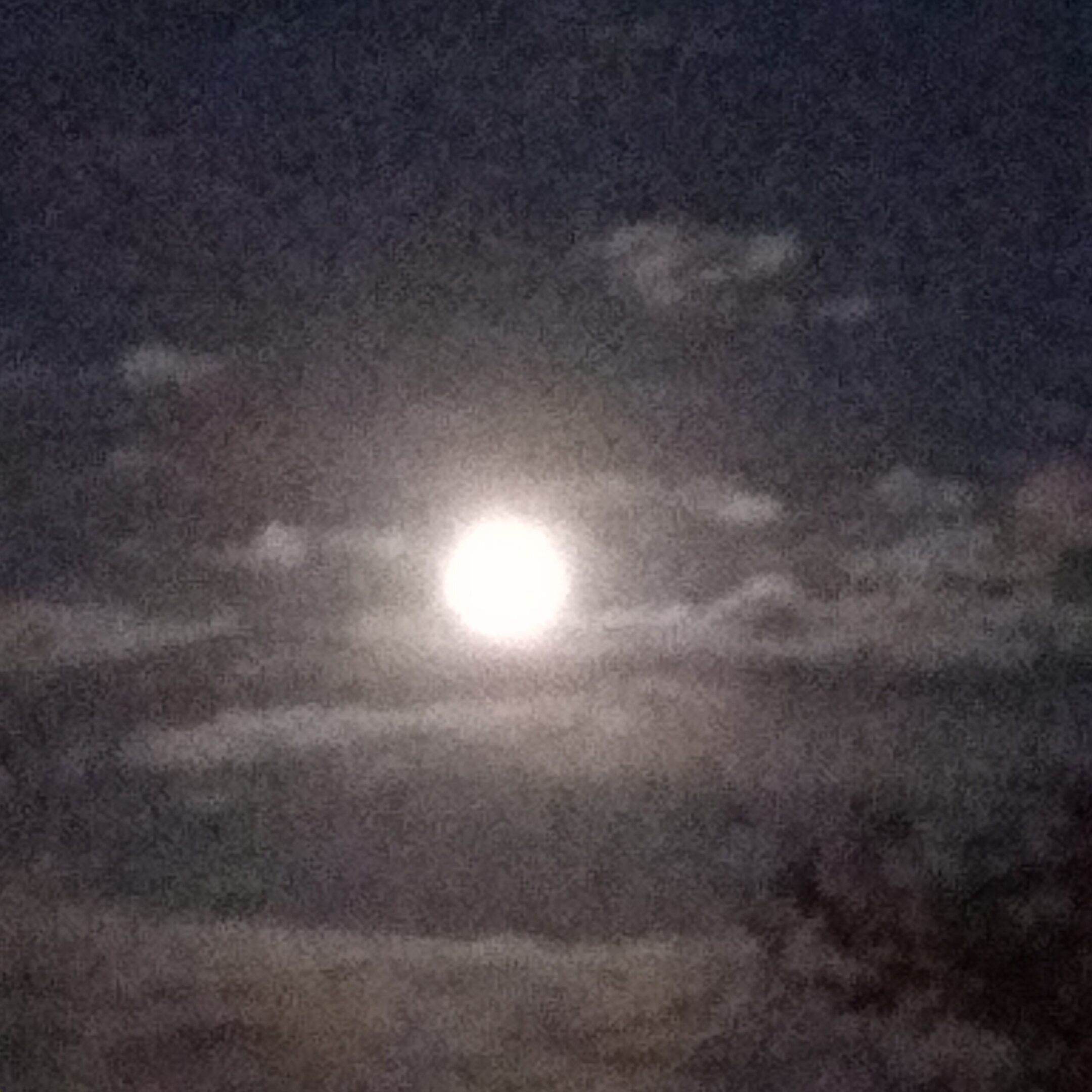 Full moon shining through cloudy night sky.