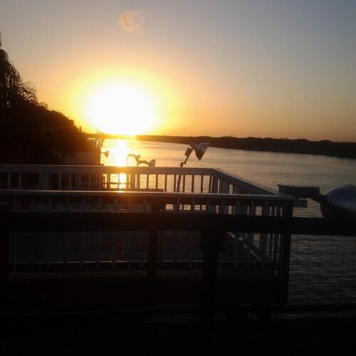 Sunset over calm water with railing view.