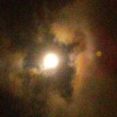 Bright moon surrounded by colorful, cloudy sky.