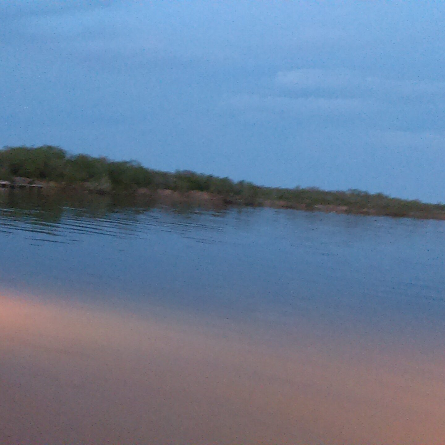 Calm lake at dusk with cloudy sky.