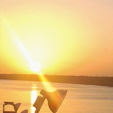 Sunset over calm water with silhouettes.