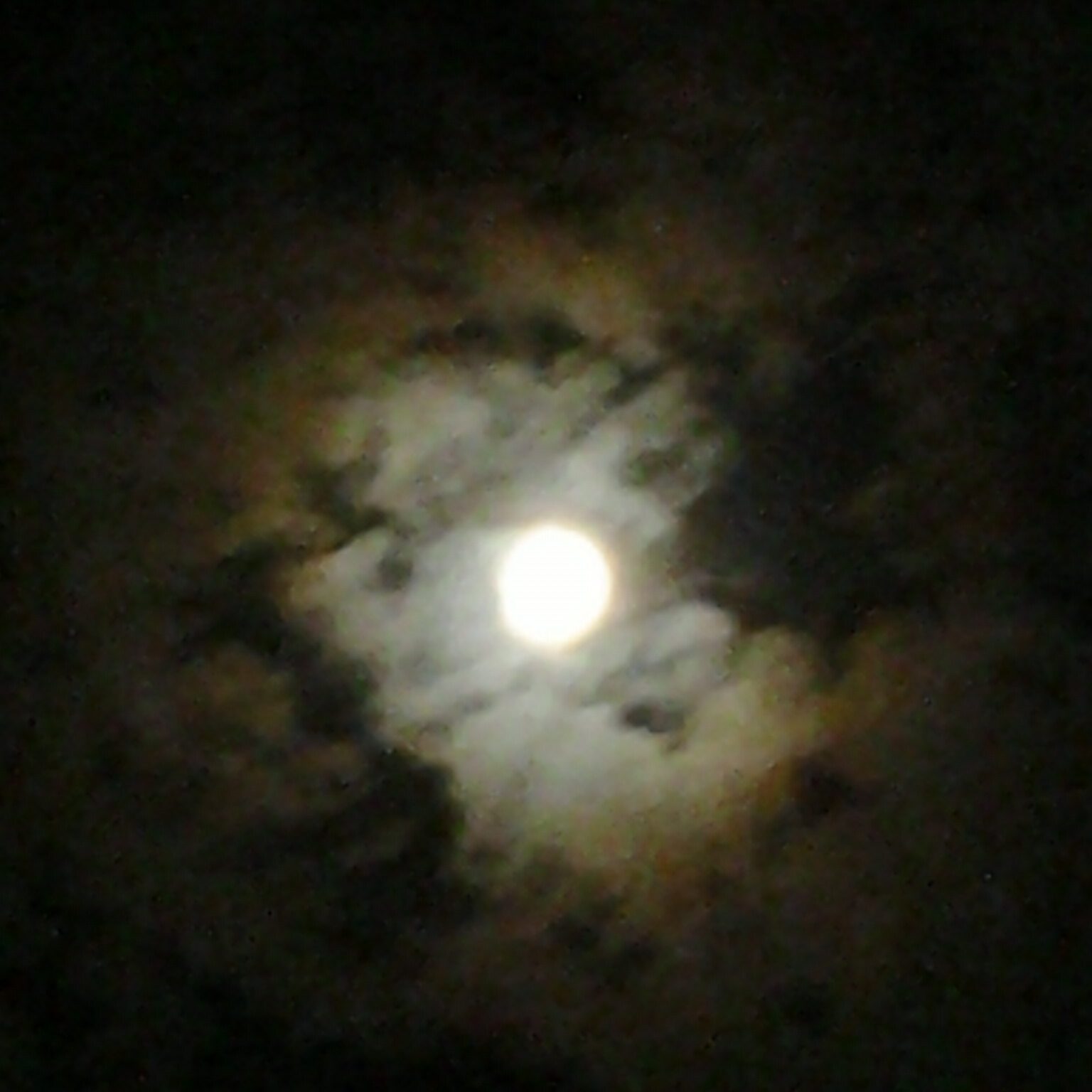 Bright moon surrounded by dark, cloudy sky.
