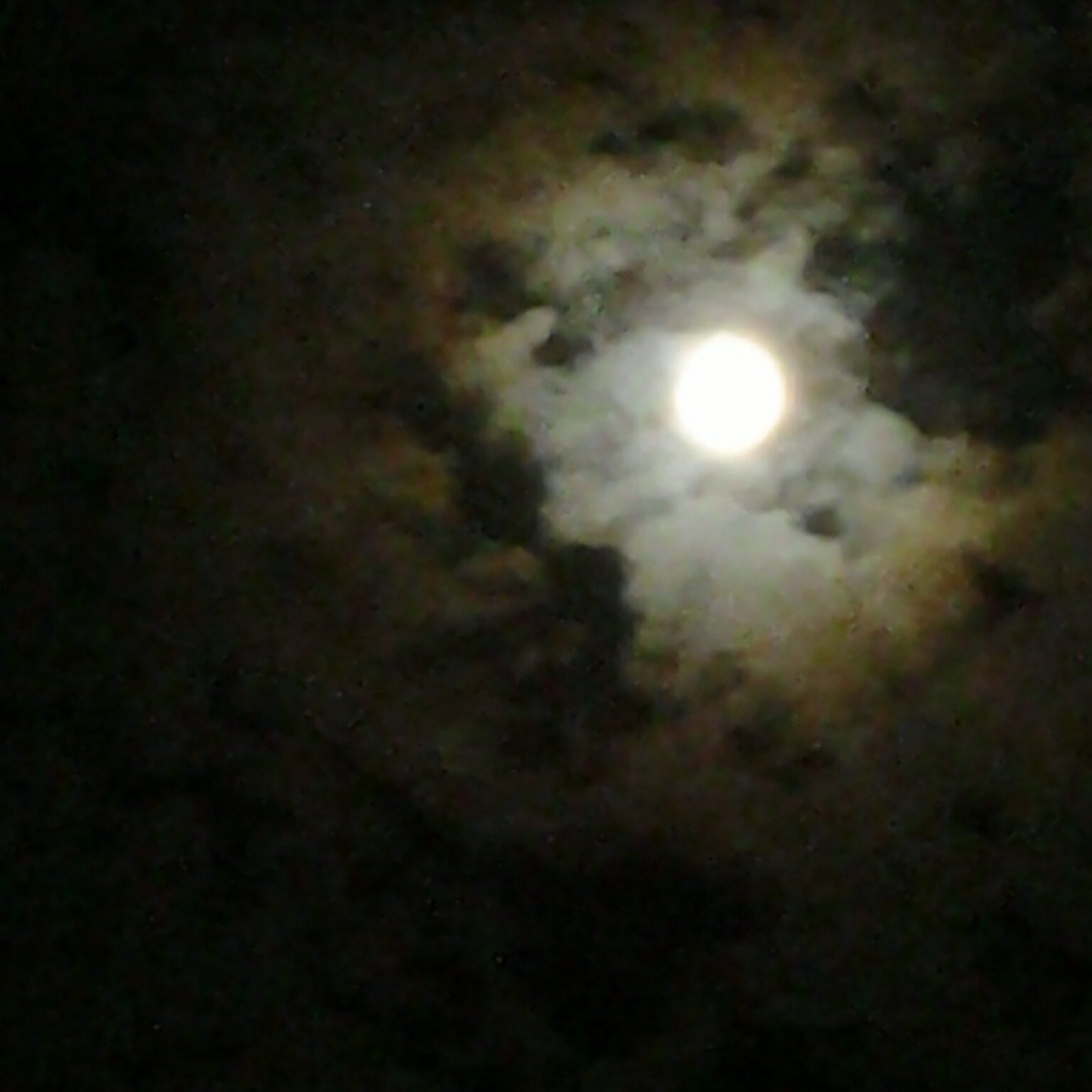 Full moon surrounded by dark, cloudy sky.