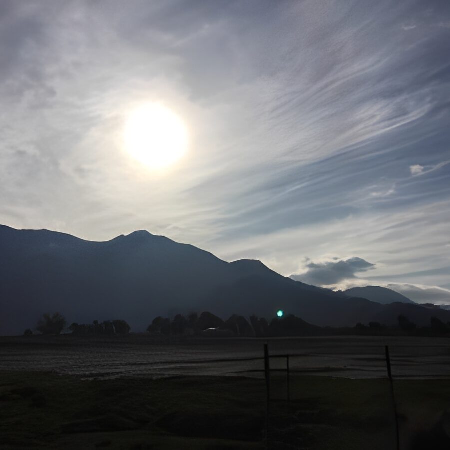 Sunset over silhouetted mountains and trees.