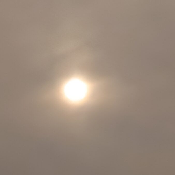 Sun obscured by hazy, cloudy sky.