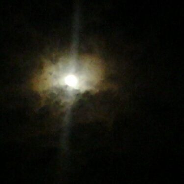 Full moon surrounded by dark, cloudy sky.