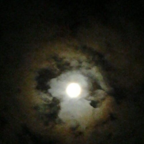 Bright full moon surrounded by dark clouds.