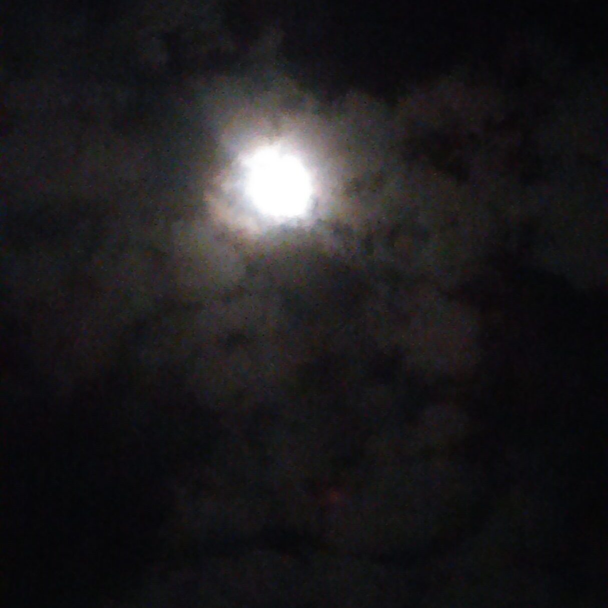 Moon shining through dark, cloudy night sky.