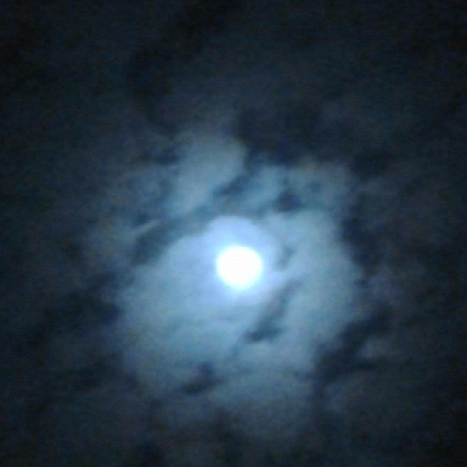 Moon shining through cloudy night sky.