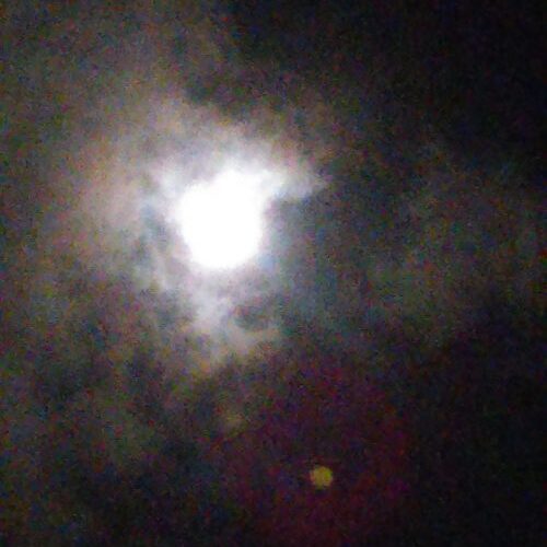 Bright moon surrounded by dark, cloudy sky.