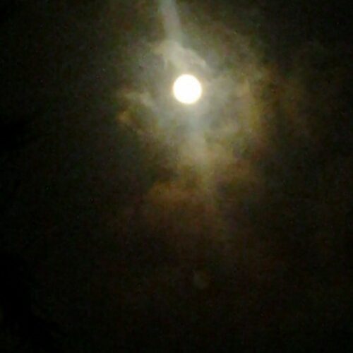 Bright moon surrounded by dark, wispy clouds.