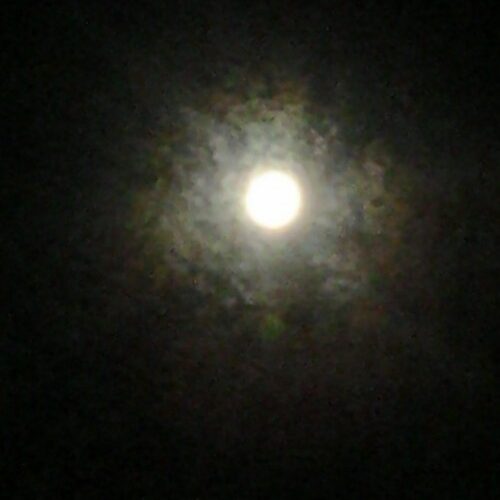 Full moon surrounded by hazy clouds.