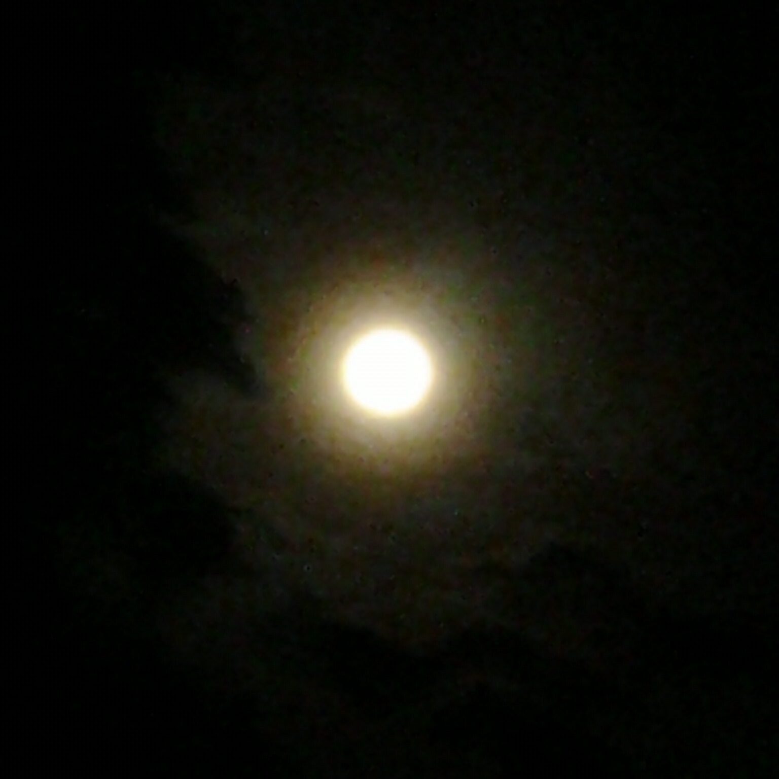 Full moon glowing in dark cloudy sky.