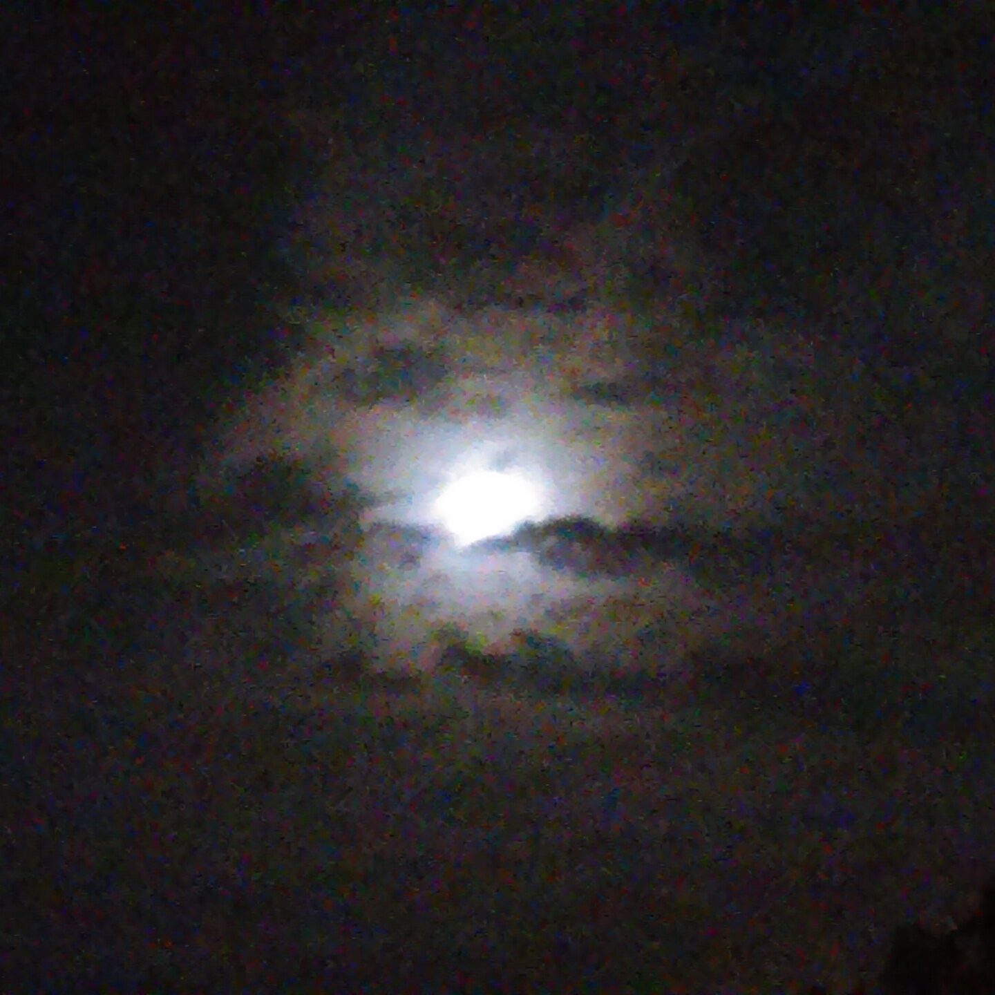 Full moon behind clouds at night.