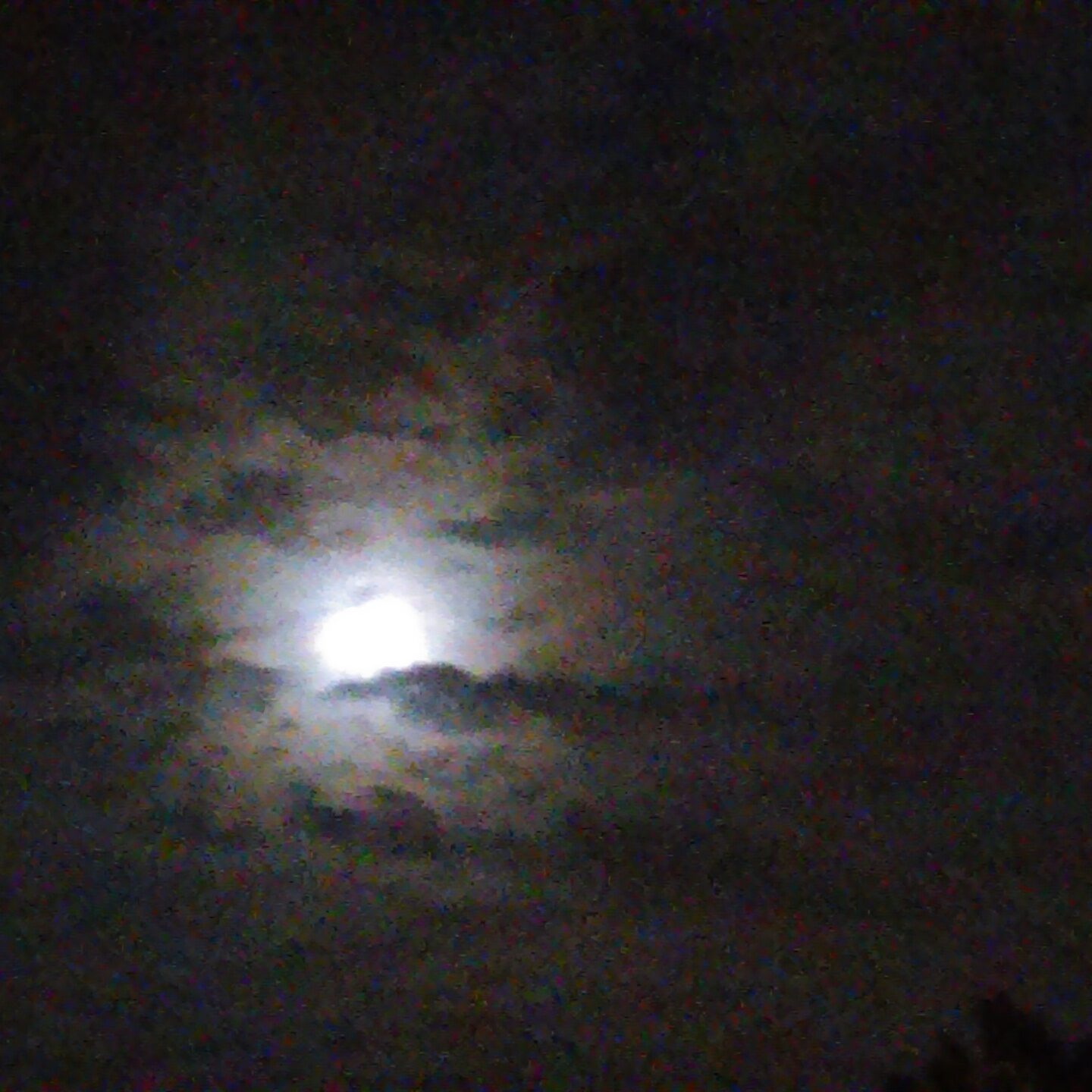 Moon shining through cloudy night sky.