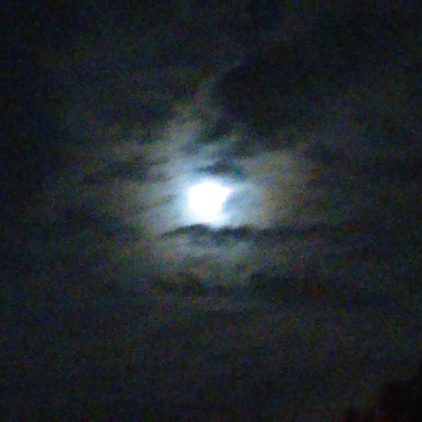 Moon shining through dark, cloudy night sky.