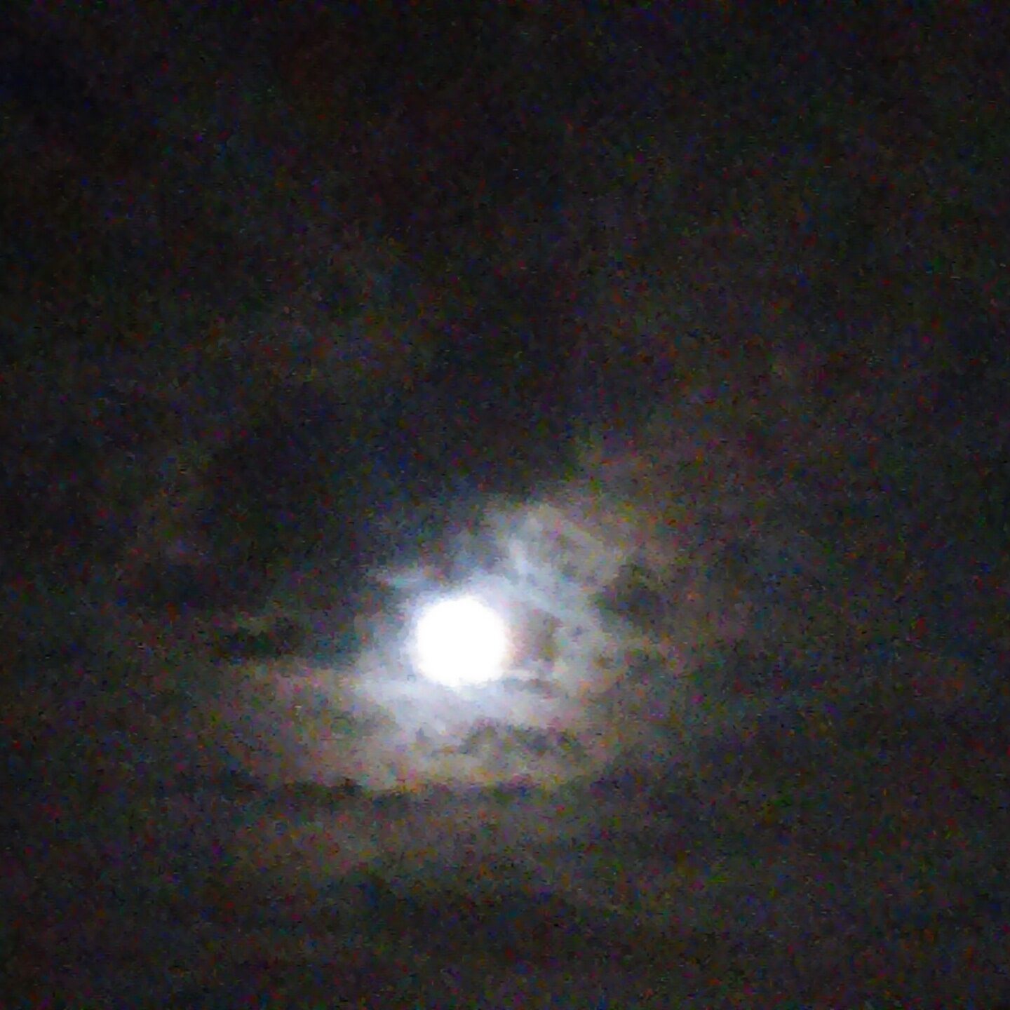 Moon shining through cloudy night sky.