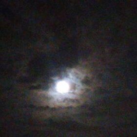 Full moon shining through dark cloudy sky.