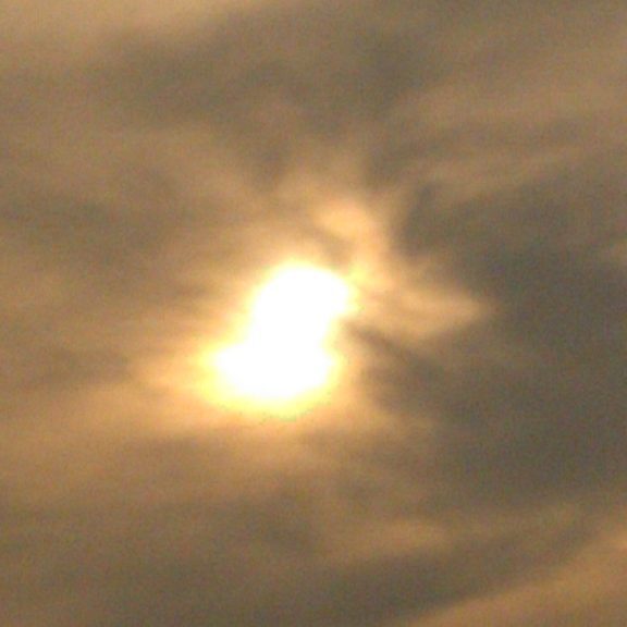Sun partially obscured by cloudy sky.
