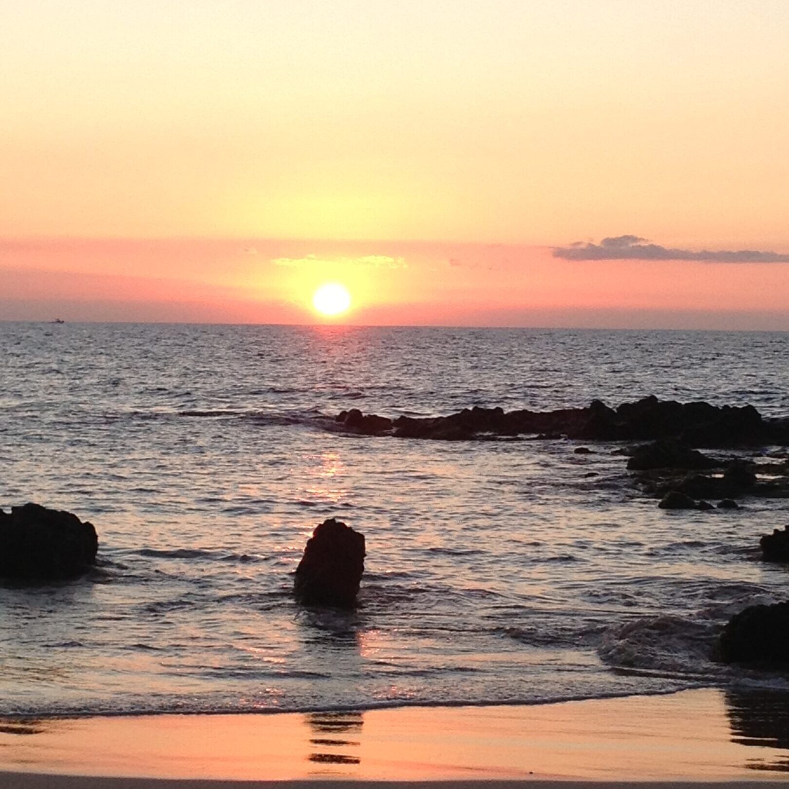 Sunset over ocean with rocky shoreline.