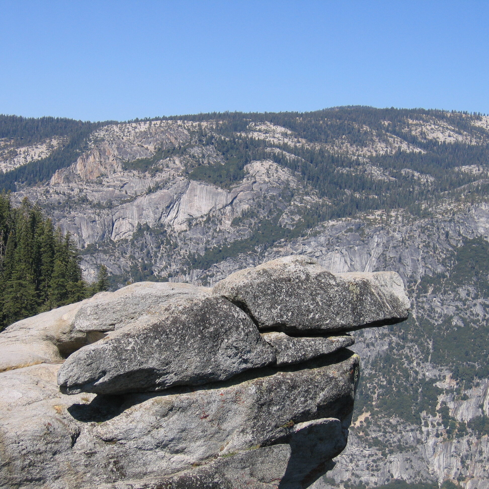 Rocky cliff overlooking mountainous landscape, clear sky.