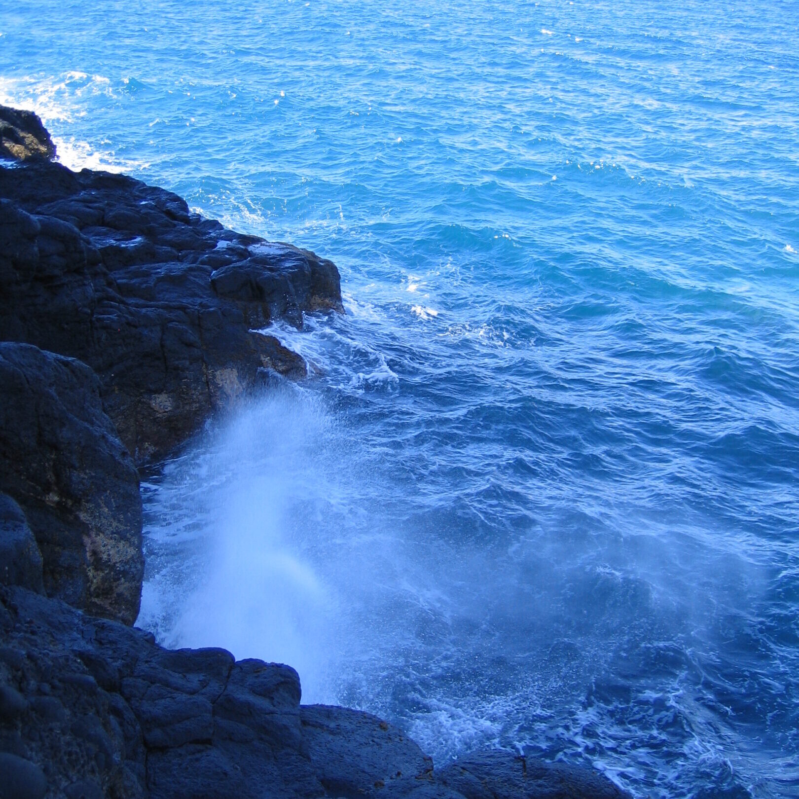 Waves crashing on rocky shoreline with ocean.