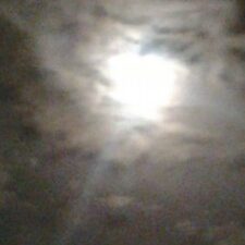 Bright moon behind cloudy night sky.