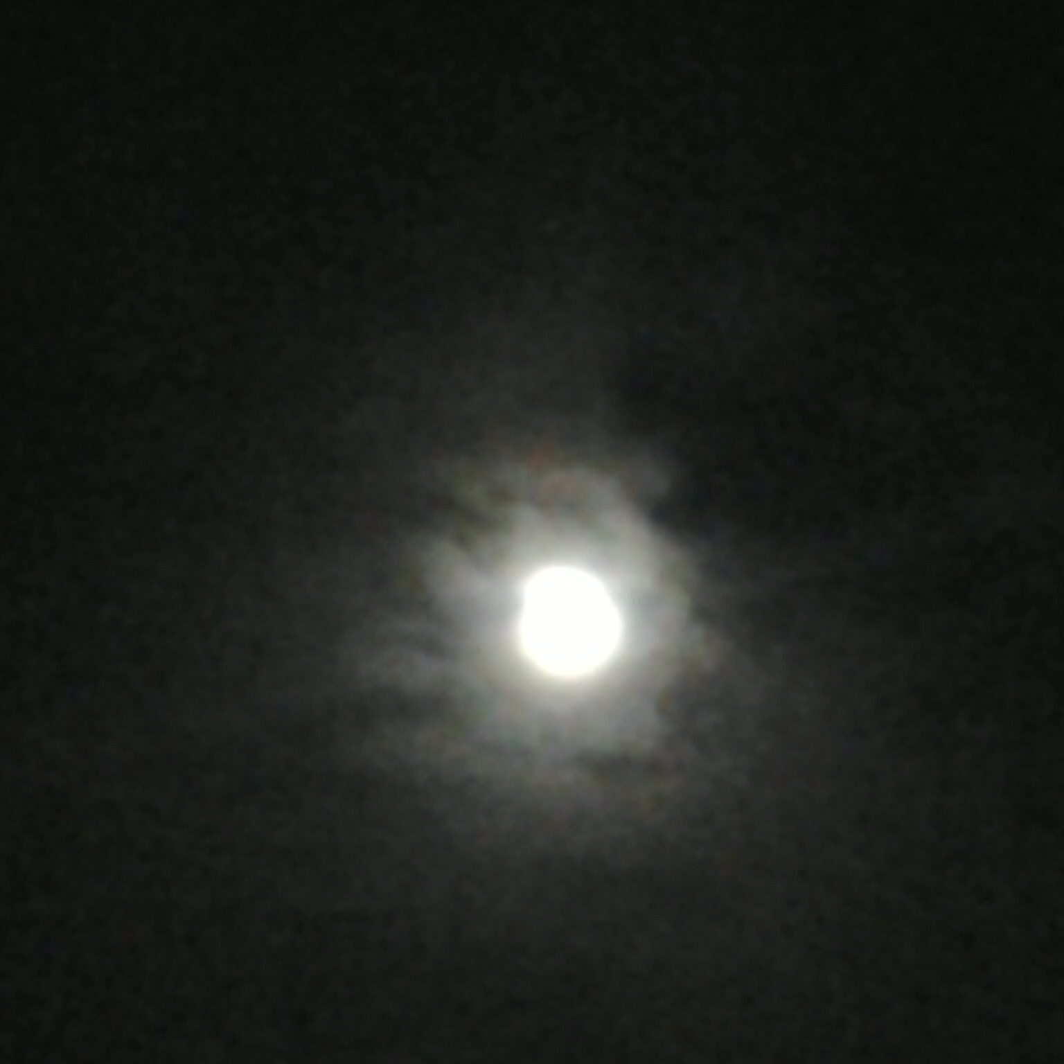 Full moon shining through cloudy night sky.