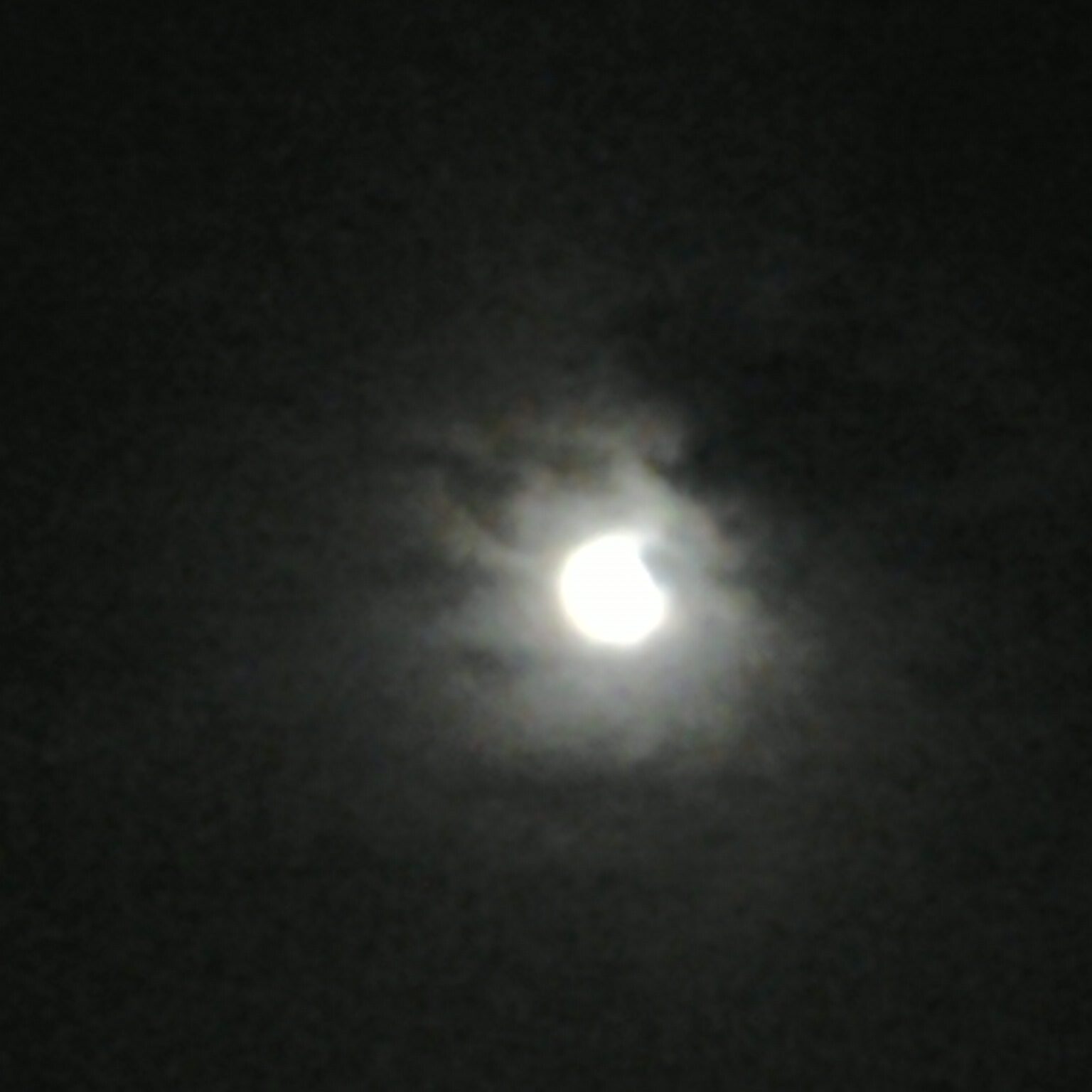 Moon obscured by clouds in night sky.