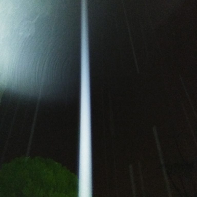 Tall light beam in dark night sky.