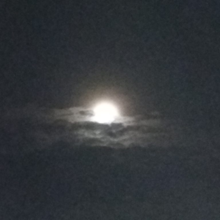 Full moon behind dark, cloudy sky.