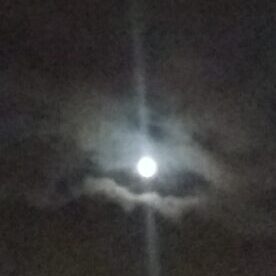 Bright moon shining through cloudy night sky.