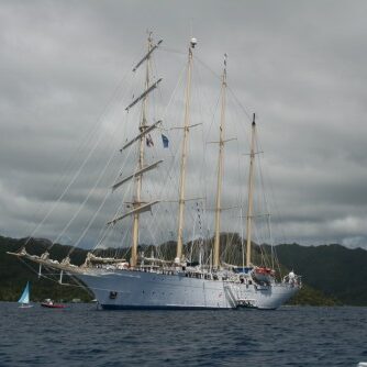 Sailing ship on calm sea near mountains.