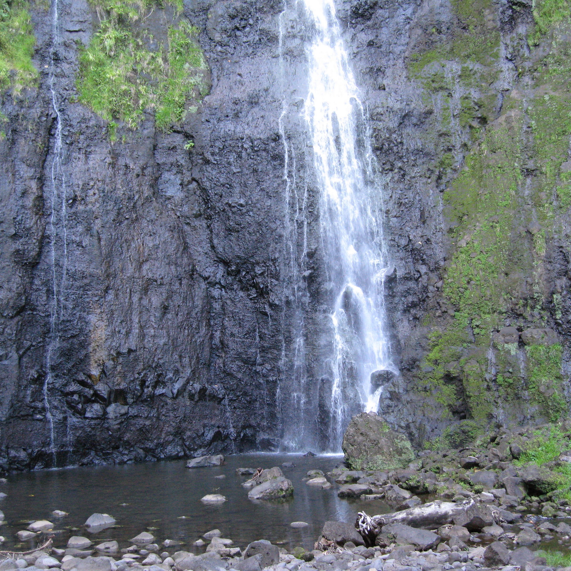 Waterfall cascading down moss-covered rocky cliff.