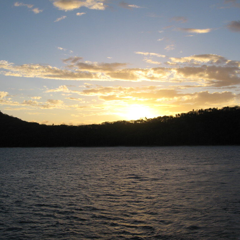 Sunset over calm lake and silhouetted hills.